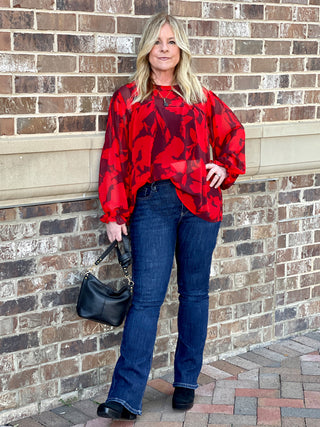 a sheer red blouse in floral print with long statement sleeves and ruffle details great for holiday fashion shown with denim