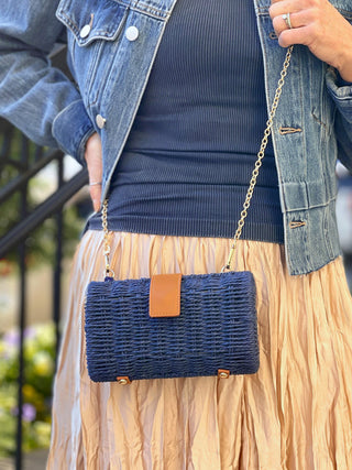 navy paper straw base clutch with magnetic snap and cross body chain paired with beige skirt and jean jacket