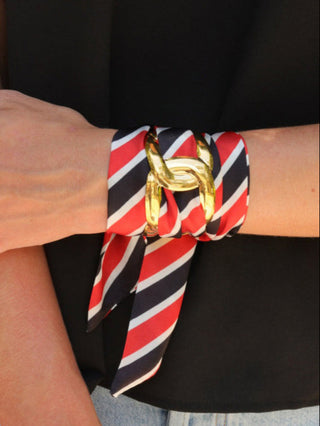 a gold stainless steel cuff threaded with a vibrant red and black striped scarf