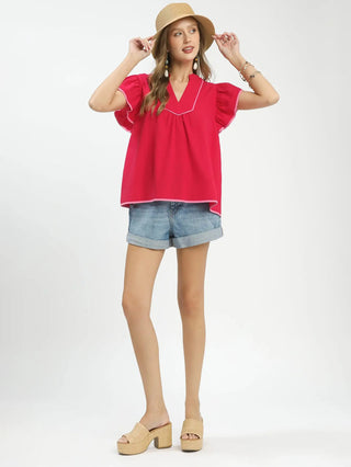 a red short sleeve ruffled top with a v neck and pink contrast piping worn with jean shorts