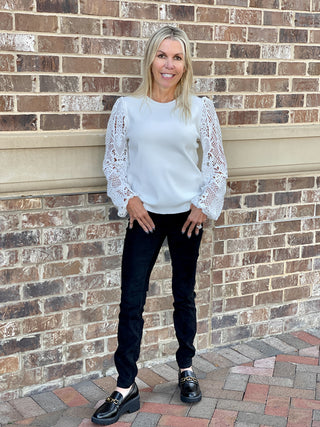 a white crew neck sweater with long lace crochet sleeves great for everyday fall and winter fashion shown with black pants