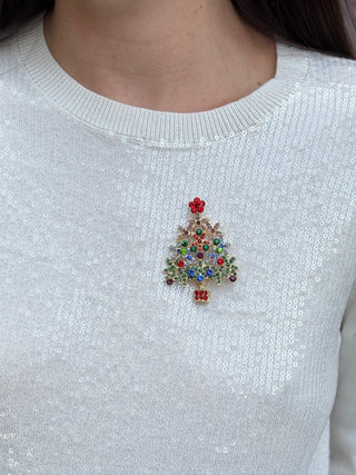 a vibrant sparkling holiday christmas tree clothing pin on a white sweater