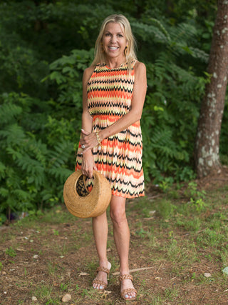 a multicolored print mini dress in shades of citrus with a sleeveless cut and cinched waist shown with tan open toed heels