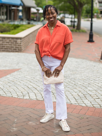 a short sleeve button up shirt in blood orange featuring a front left pocket and hi lo hem shown with white pants