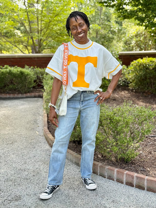 a boxy white short sleeve tee sweatshirt with a tennessee orange t on the front worn with blue jeans