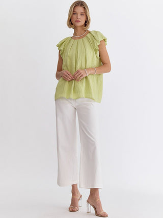 ruffled short sleeve honeydew color top with round neck and playful twist worn with white pants