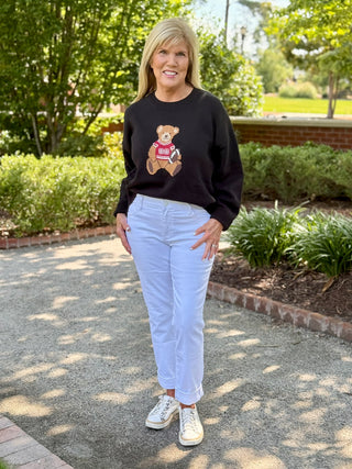a black and red graphic sweater with a football playing teddy bear on the front worn with white jeans