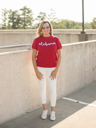 a red sweater tshirt with white glitter text that reads alabama perfect for bama football fans shown with white pants
