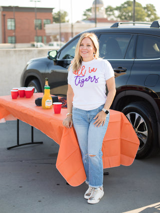 a white sweater tshirt with orange and purple glitter text that reads all in tigers made for clemson fans with denim pants