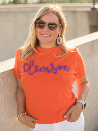 an orange sweater tshirt with purple glitter text that reads clemson perfect for clemson tigers football fans