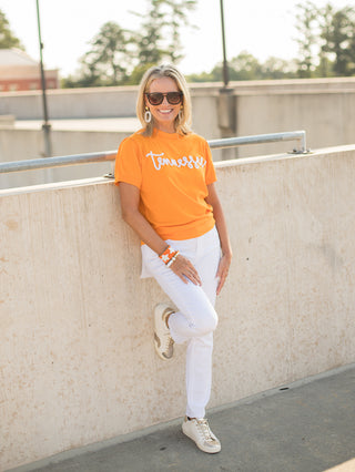 an orange sweater tshirt with white glitter text that reads tennessee made for vols football fans with white pants