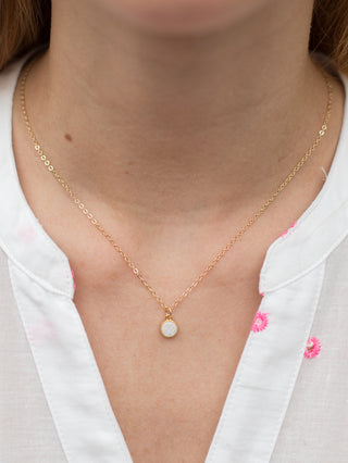 a gold necklace with a white druzy stone along the dainty cable chain 
