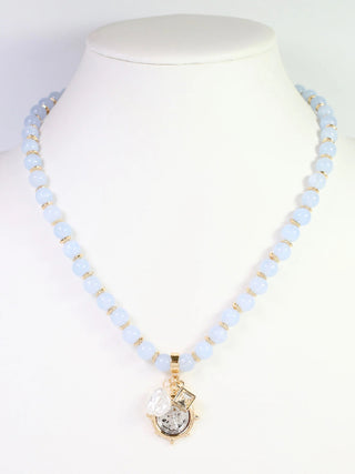 Necklace with light blue beads and a gold pendant on a mannequin.
