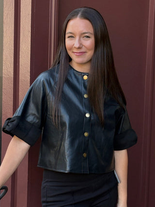 a black faux leather short sleeve jacket with front buttons and suede trim