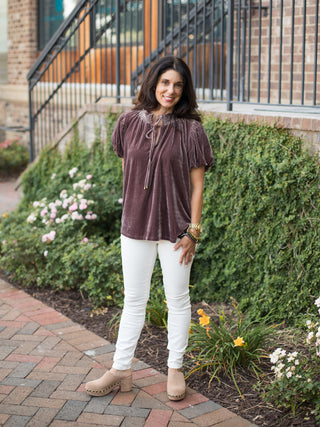 a dark purple velvet top with puff sleeves and feminine ruffles perfect for feminine fall fashion shown with white pants