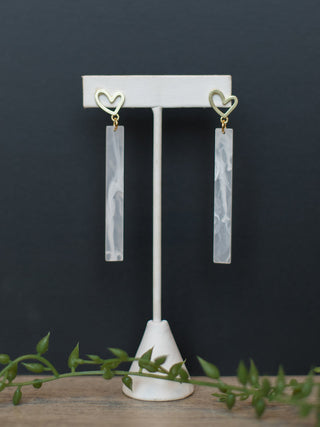 a pair of white acrylic bar earrings with yellow gold hearts