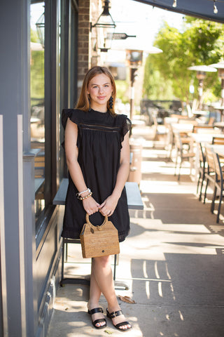 a black ruffled sleeve dress with a relaxed fit and lace trim detailing along the neck and hem shown with black sandals