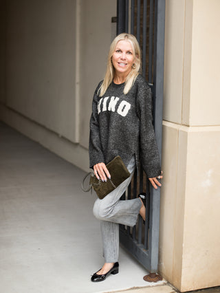 a dark grey oversize sweatshirt with vino written across in white perfect for wine lover gifts shown with denim