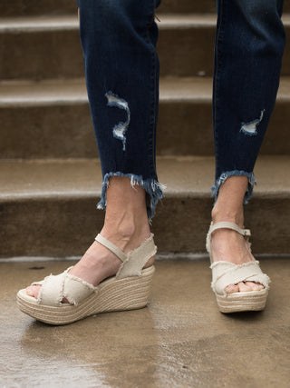 a criss cross peep toe wedge in light beige with ankle straps and an espadrille platform