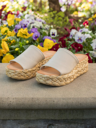 a pair of slip on sandals with sand hued leather and boho chic raffia