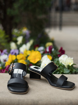 Slip on black leather block heel sandal with wide buckled straps gold grommet detail and square toe side view