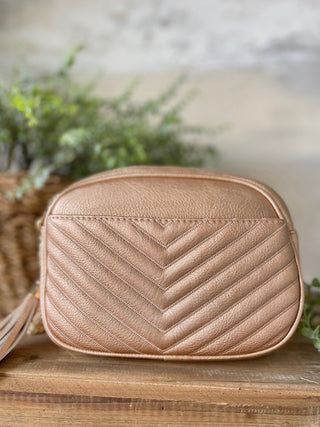 a rose gold purse with adjustable straps and v pattern stitching made of vegan leather with gold hardware and tassel zippers