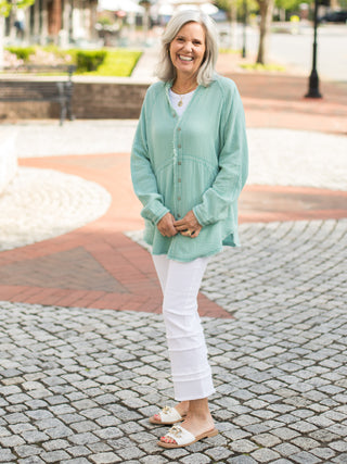 teal green breezy cotton tunic button down shirt with v-neckline and frayed edges is made of 100% cotton worn with white denim