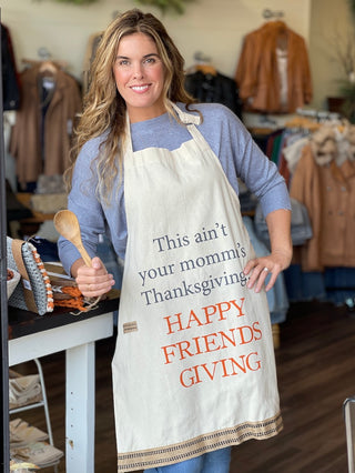 an off white apron that reads this ain't your mommas thanksgiving happy friendsgiving with a matching spoon