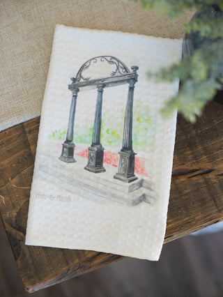 an off white tea towel featuring a watercolor of the university of georgia arches atop waffle weave fabric