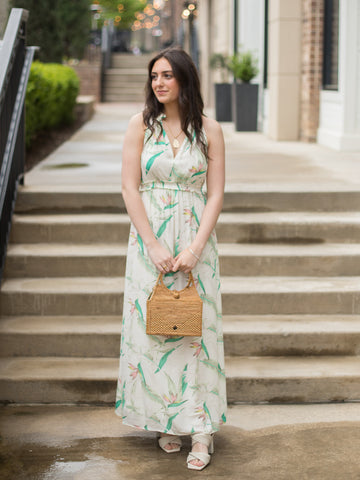 woman wearing cream colored sleeveless maxi dress with green floral pattern ruffle details and lined long skirt